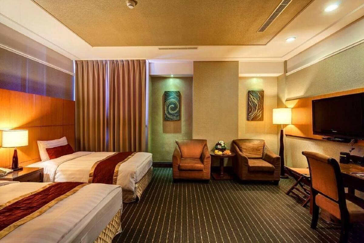 Ein Hotelzimmer mit zwei Betten, einem Schreibtisch, einem Fernseher und einem Sessel.