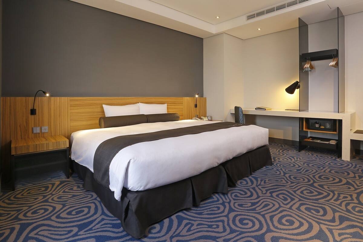 Ein Hotelzimmer mit einem großen Bett, einem Schreibtisch, einem Stuhl und einem Spiegel.