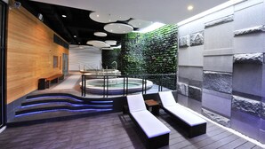 Un moderno espacio de spa con un jacuzzi, sillas de descanso y una pared de madera.