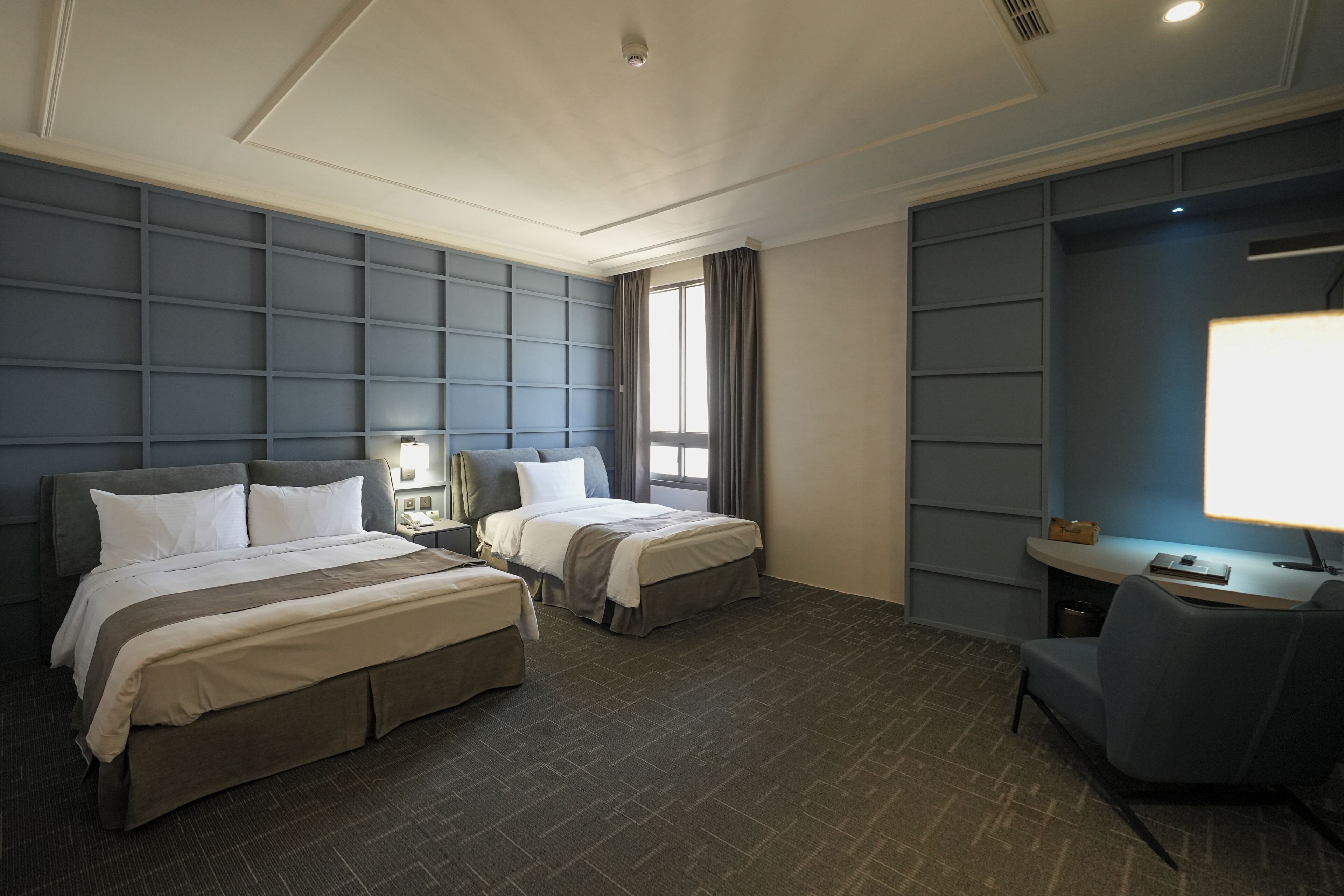 Een hotelkamer met twee bedden, een bureau, een stoel en een groot raam.