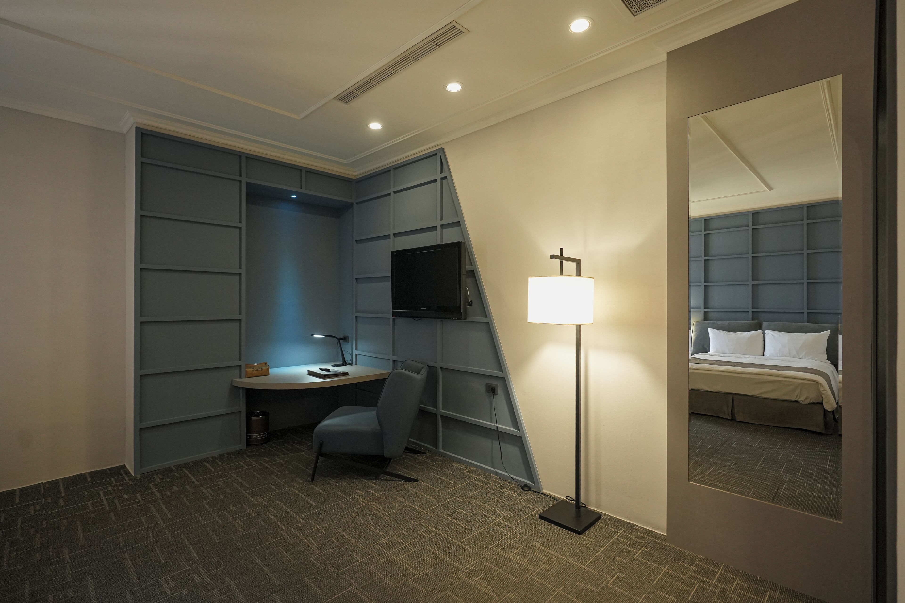Habitación de hotel con escritorio, silla, lámpara, televisor y cama con cabecero.