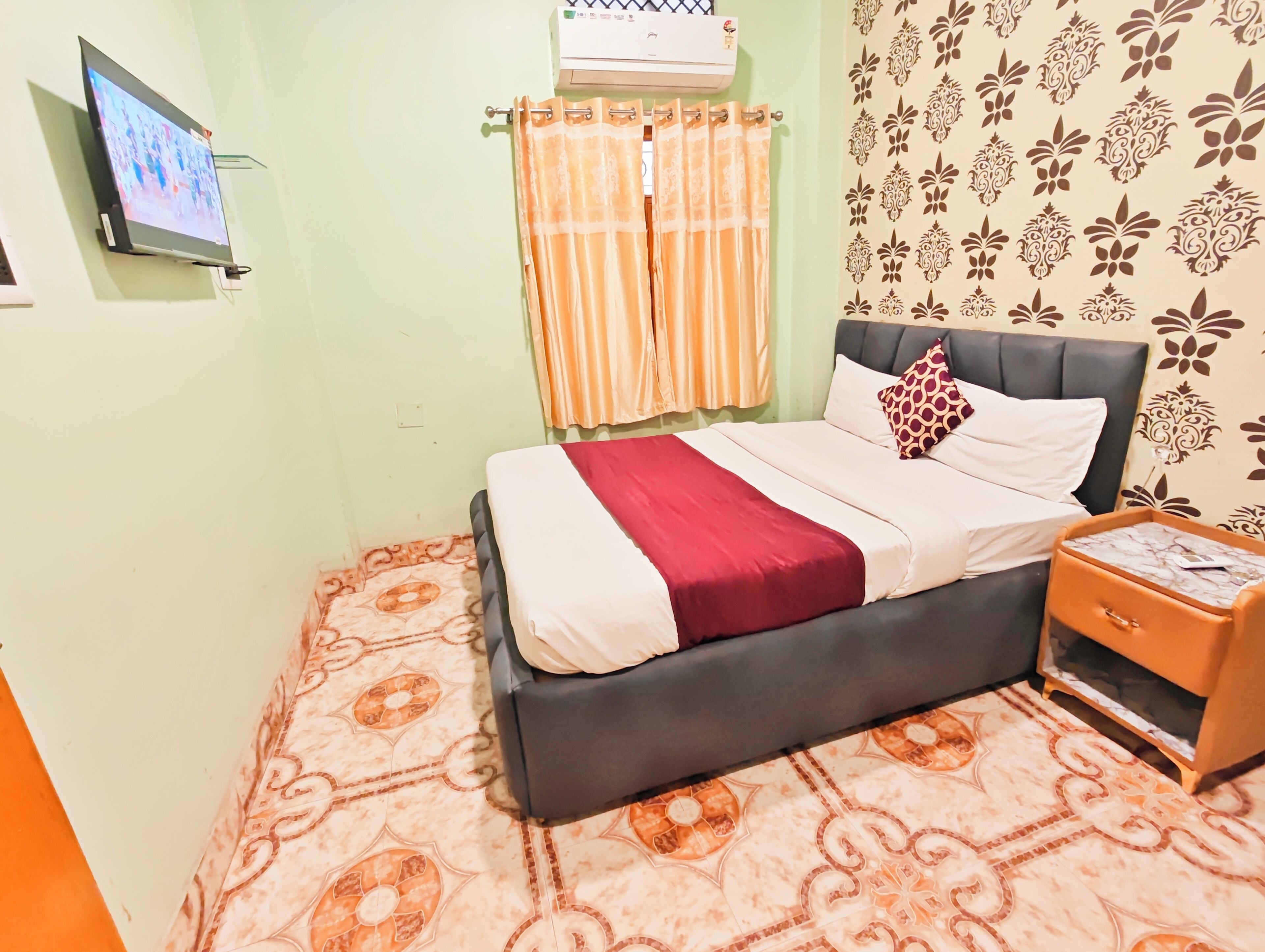 Un dormitorio con cama, mesita de noche, televisor y pared con diseño.