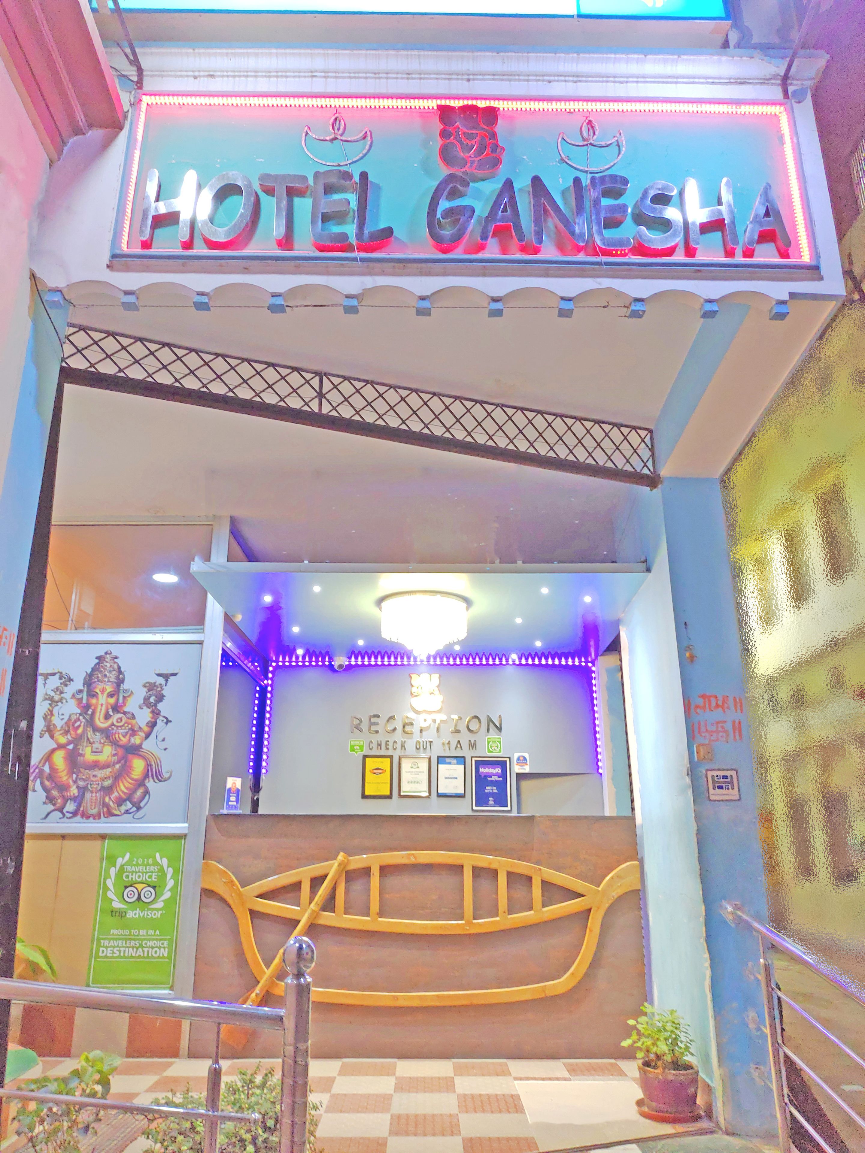 La entrada del Hotel Ganesha, con mostrador de recepción y mostradores de salida, y un cartel que indica la hora de registro de salida.