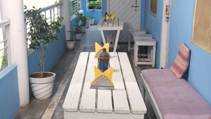 A covered outdoor seating area with white wooden tables and benches, potted plants, and a small lantern. - Shri Yoga Mandir Guest House (Varanasi)