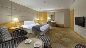 A hotel room with a bed, two bedside lamps, a TV, a desk, and a chair.