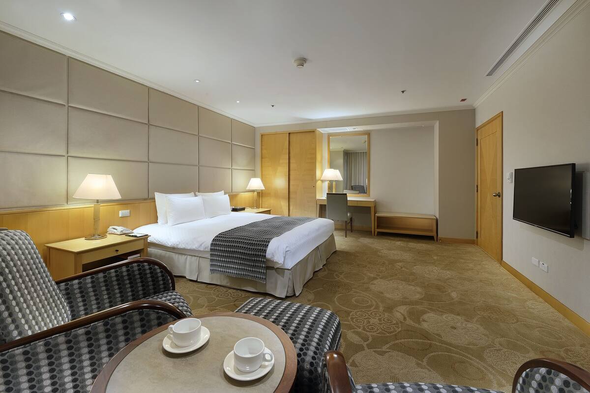 Una habitación de hotel con una cama, dos lámparas de noche, un televisor, un escritorio y una silla.