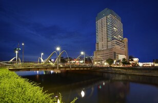 Un puente moderno con arcos singulares sobre un río tranquilo, que refleja las luces de la ciudad.