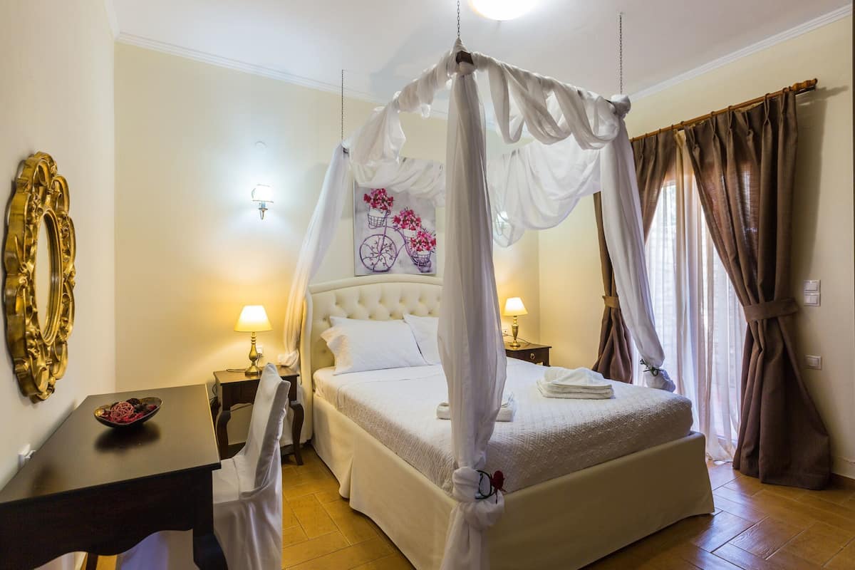 A bedroom with a four-poster bed, a bedside table with a lamp, a decorative mirror, and a wall art piece.