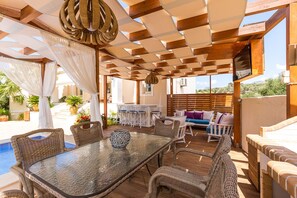 An outdoor patio area with a glass table, wicker chairs, a pool, and a seating area with cushions. - Cretan Residence Mediterranean Luxury Private Villas (Mylopotamos)