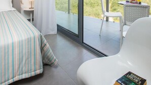 Ein Schlafzimmer mit Bett, Stuhl, Tisch und Blick auf eine Landschaft durch eine Schiebetür.