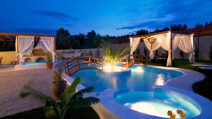 Ein Pool mit Holzterrasse, umgeben von Topfpflanzen und einem Pavillon mit weißen Vorhängen.