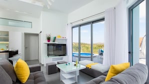 Ein modernes Wohnzimmer mit einer Couch, einem Glastisch und Blick auf einen Swimmingpool.