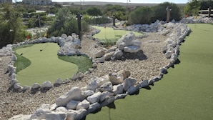 Un parcours de minigolf doté d’un tapis vert, entouré de rochers blancs et de verdure.