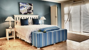 Une chambre à coucher comprenant un lit, deux tables de chevet, une commode, une fenêtre avec des stores et une porte.