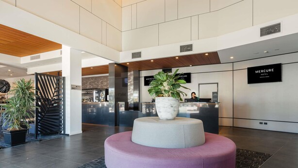 Un hall d’hôtel moderne avec un comptoir d’accueil, une grande plante en pot et un espace salon circulaire original.