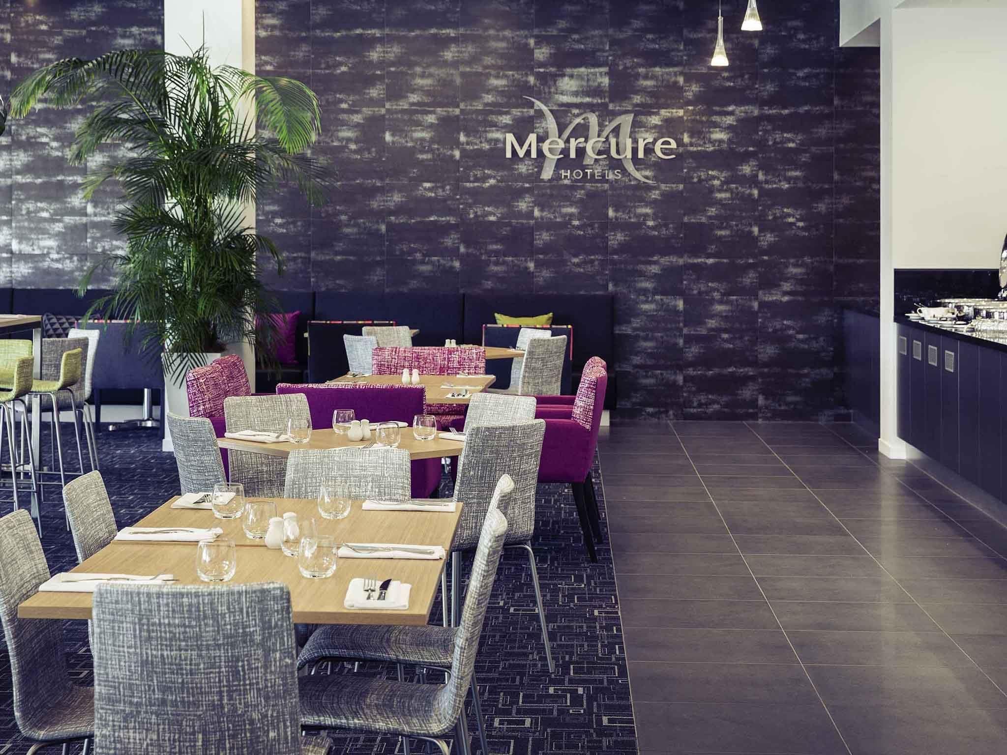 A modern dining area with a dark textured wall, a large potted plant, and a mix of grey and purple upholstered chairs.