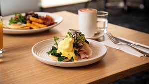 A breakfast setting with a plate of eggs benedict, a glass of orange juice, and a cup of coffee on a wooden table.