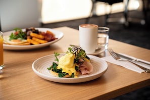 Un desayuno con un plato de huevos Benedict, un vaso de jugo de naranja y una taza de café sobre una mesa de madera.