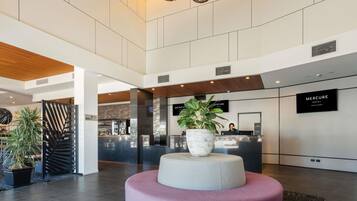 A modern hotel lobby with a reception desk, a large potted plant, and a unique circular seating area.