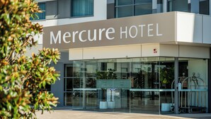 L’entrée d’un hôtel Mercure, avec une façade en verre, un comptoir d’accueil et des plantes en pot.