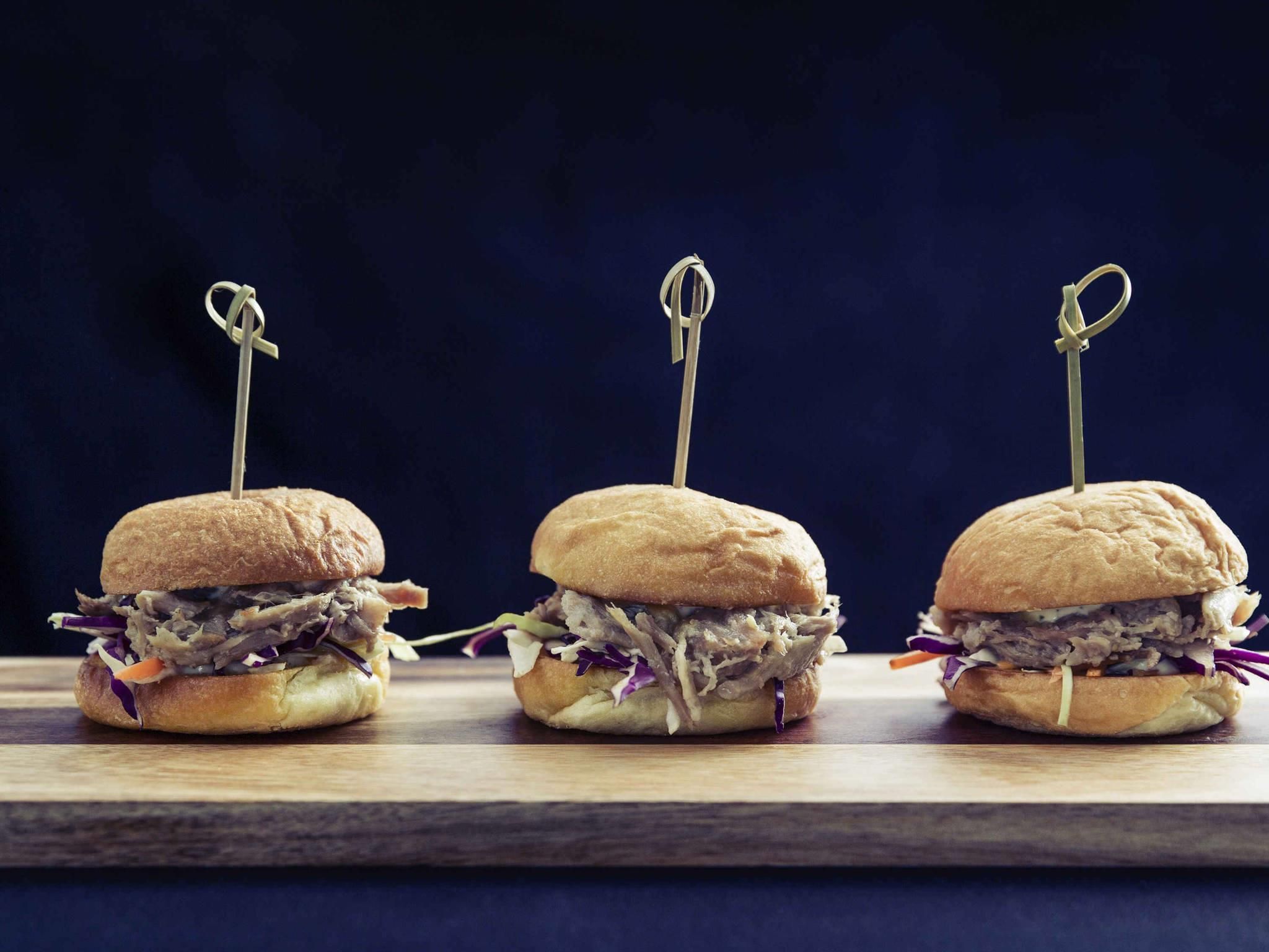Trois sandwichs maintenus par des cure-dents, présentés sur une planche en bois, le tout sur un fond sombre.