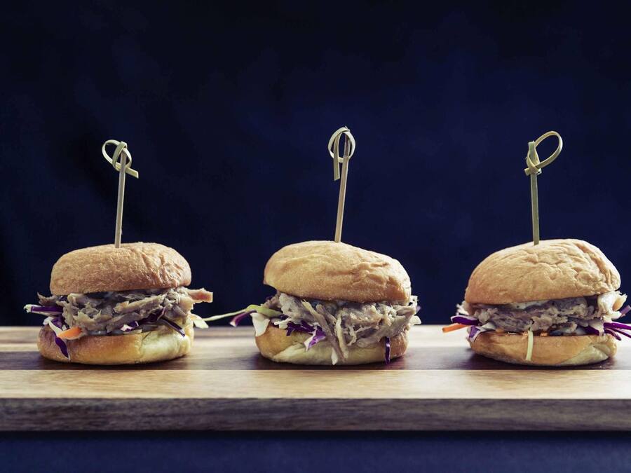 Three sandwiches with toothpicks on a wooden board against a dark background.
