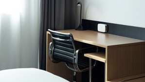 A hotel room with a wooden desk, a black leather chair, a desk lamp, and a power outlet.