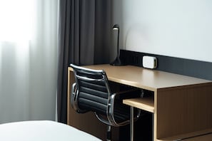Habitación de hotel con un escritorio de madera, una silla de cuero negro, una lámpara de escritorio y un enchufe.