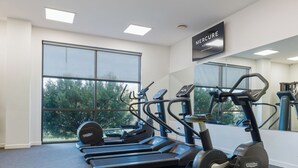 Un gimnasio con cintas de correr, elípticas y un amplio ventanal con vistas a árboles.