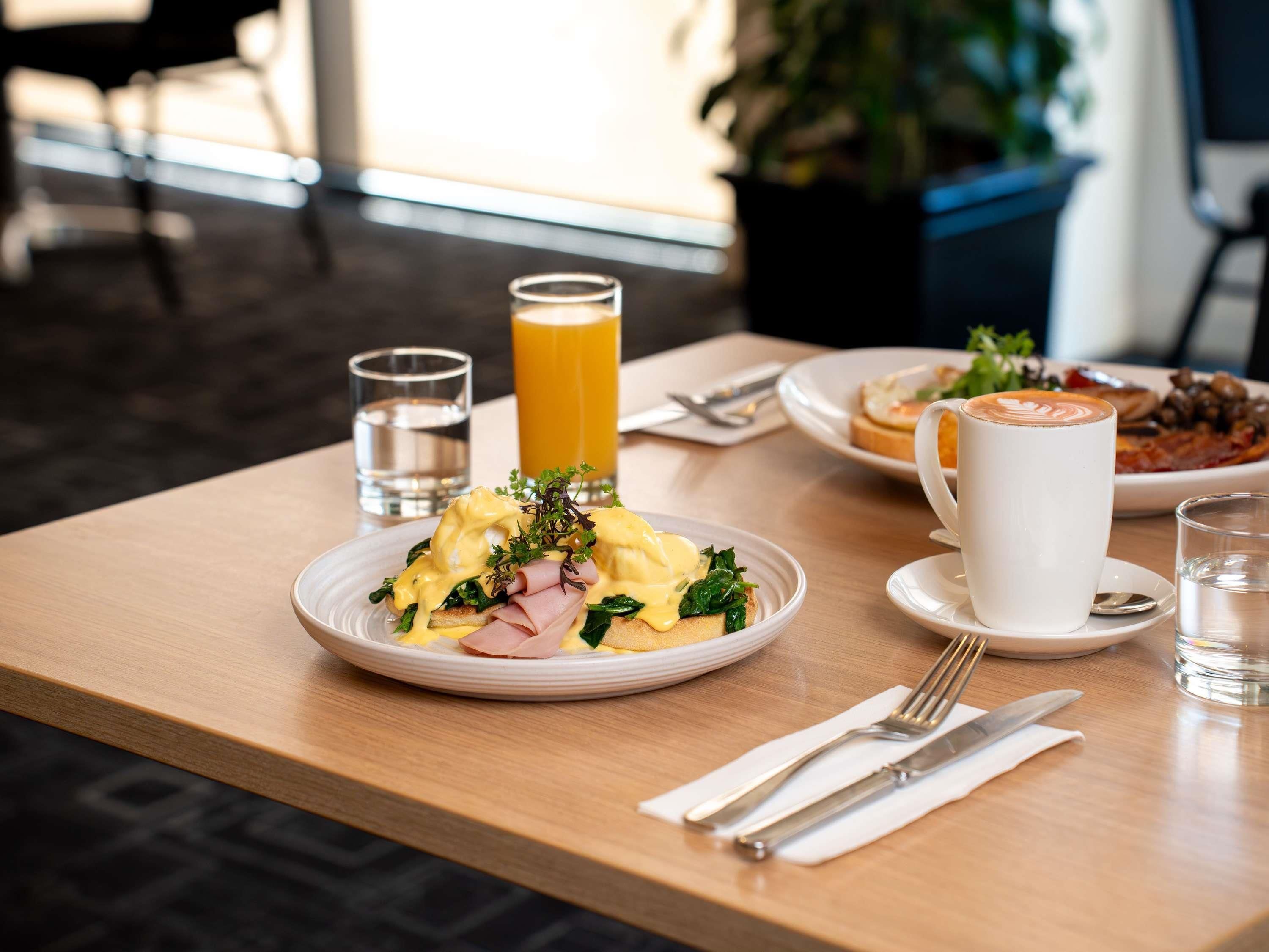 A breakfast setting with a plate of eggs benedict, a glass of orange juice, and a cup of coffee on a wooden table.