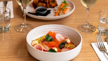 A dining table with a bowl of food, two glasses of white wine, and a fork on a napkin.