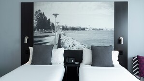 Habitación de hotel con cama, dos almohadas, mesita de noche con teléfono y una amplia vista en blanco y negro de un paisaje urbano.