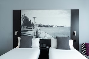 Habitación de hotel con cama, dos almohadas, mesita de noche con teléfono y una amplia vista en blanco y negro de un paisaje urbano.