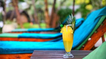 A tropical drink on a wooden table with a blurred background of lounge chairs and greenery.