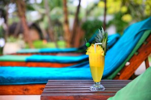 Une boisson tropicale sur une table en bois, avec en arrière-plan flou des chaises longues et de la verdure.