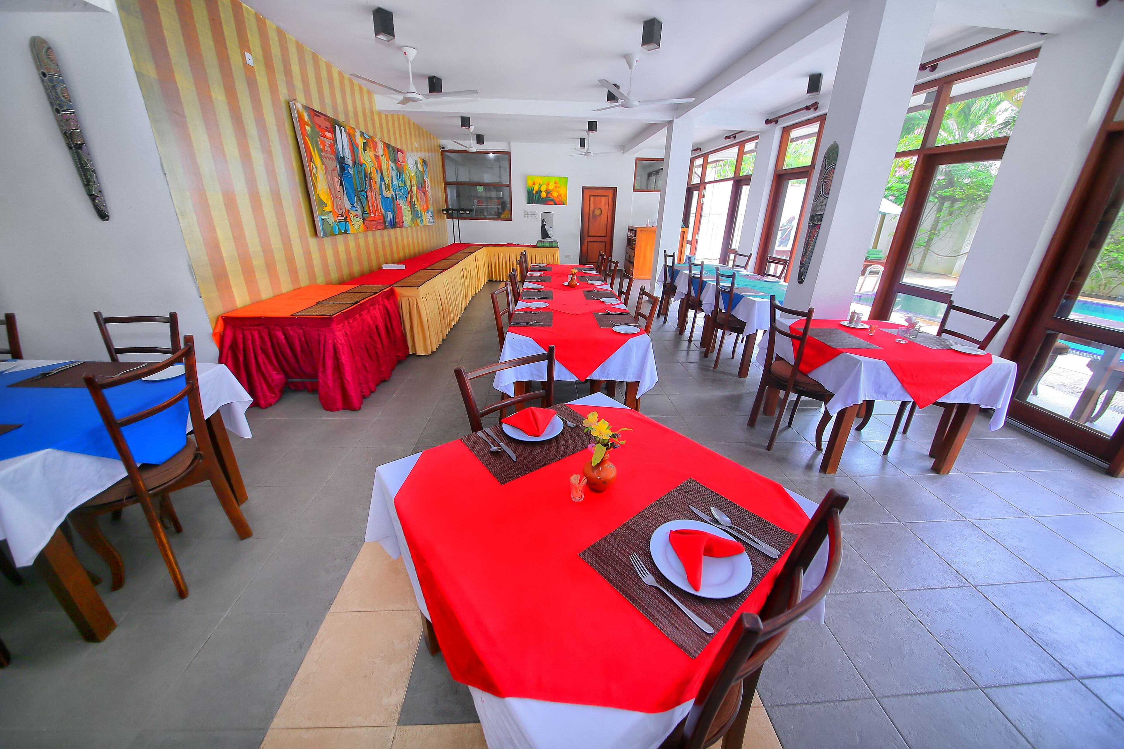 A dining area with multiple tables, each covered with a red tablecloth and set with white plates, cutlery, and napkins.
