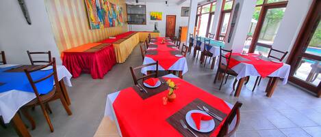 A dining area with multiple tables, each covered with a red tablecloth and set with white plates, cutlery, and napkins.