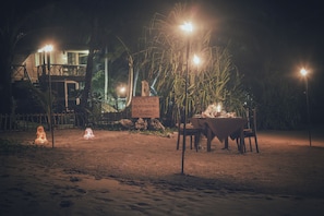 A beachside dining area with a sign for Rockside Beach Resort, surrounded by palm trees and a wooden fence.