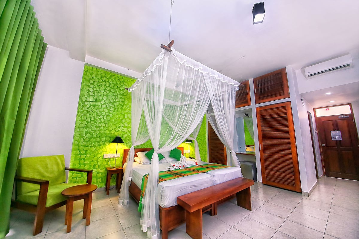A room with a bed, a bench, a green chair, a bedside table, and a wall with a green mosaic pattern.