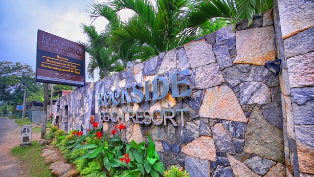 Señal de Rockside Beach Resort con servicios indicados, incluyendo habitaciones, restaurante y bar, piscina y spa, y una URL de sitio web.