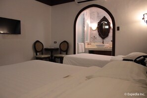 A hotel room with two beds, a small table, two chairs, a sink, and a mirror.