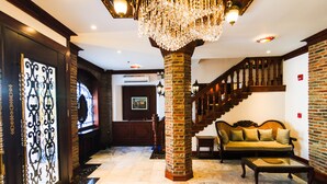 A lobby with a marble floor, a chandelier, a brick column, a staircase, and a sofa. - Hotel Luna Annex (Vigan)