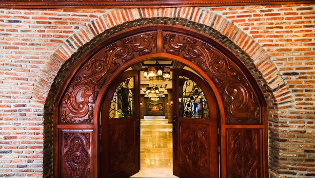 An ornate wooden archway leading to a lobby with a chandelier and a view of a room in the background. - Hotel Luna Annex (Vigan)