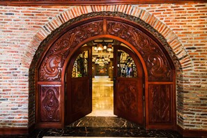Ein verziertes hölzernes Tor führt zu einer Lobby mit einer Chandelier und Blick auf einen Raum im Hintergrund.