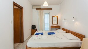 Une chambre d’hôtel avec un lit, une tête de lit en bois, une table de chevet avec une lampe, un miroir et une fenêtre avec des rideaux.