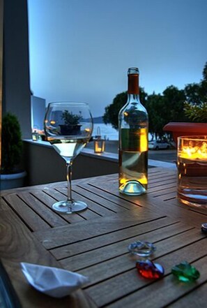 A wooden table with a bottle of white wine and a wine glass, set against a backdrop of a clear sky and distant trees. - Marathakis Apartments (Chania)