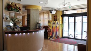 A reception area with a curved reception desk, a large window with a view of the street, and a red carpet leading to the entrance. - Hotel Cristal Eboli (Eboli)