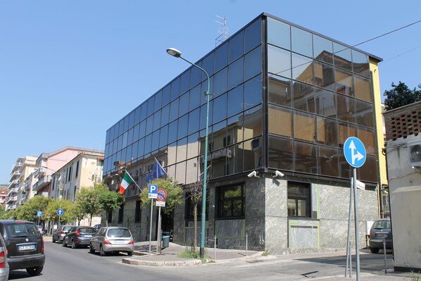 Un edificio moderno con fachada de vidrio, coches aparcados y cielo despejado.