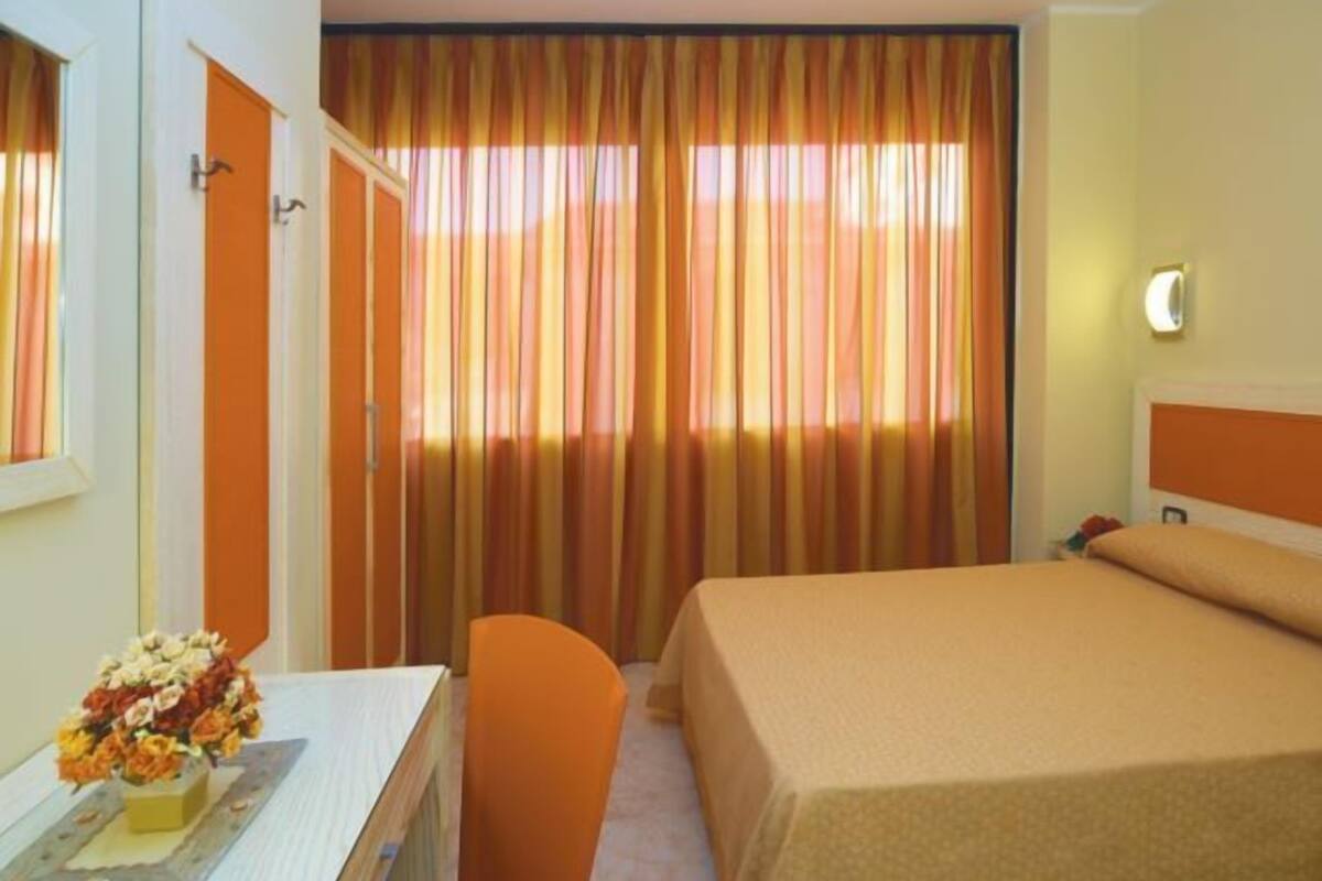 Hotelkamer met een bed, een bureau met stoel, nachtkastje en raam met gordijnen.