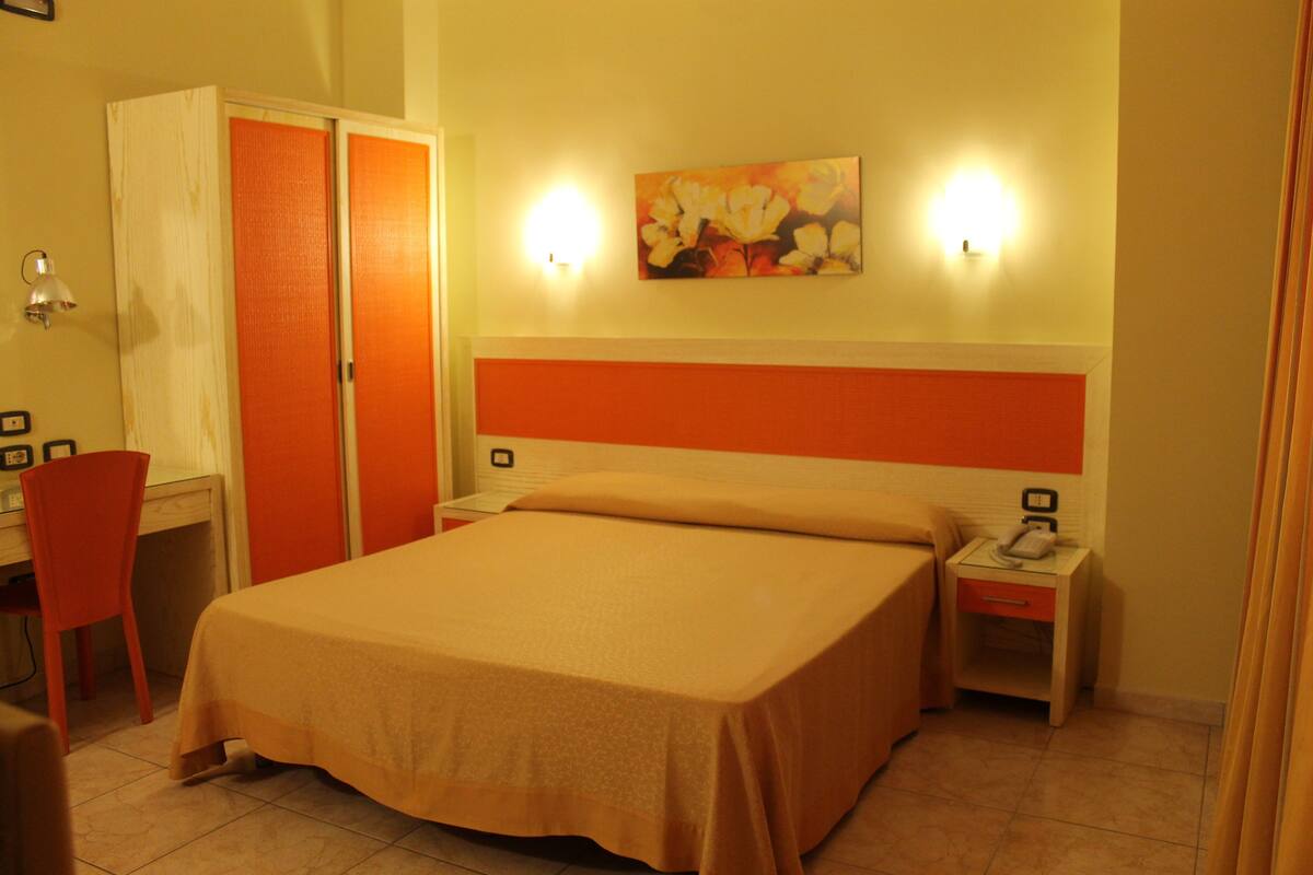 Een hotelkamer met een bed, een bureau, een stoel en een nachtkastje met een telefoon.